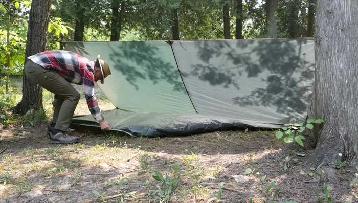 Pass the remaining half of the tarp under the lean-to and stake it down.