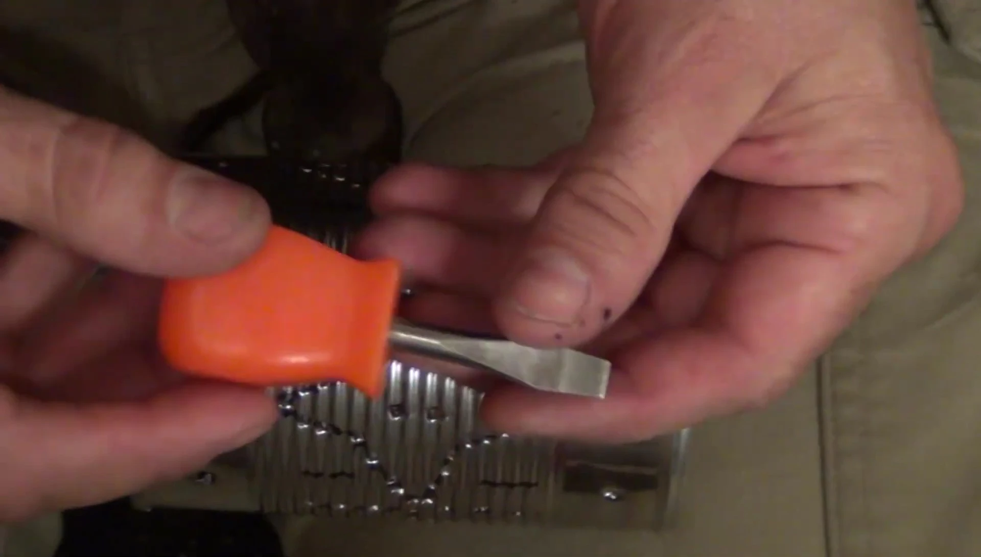 Using a flathead screwdriver to punch holes in the tin can.